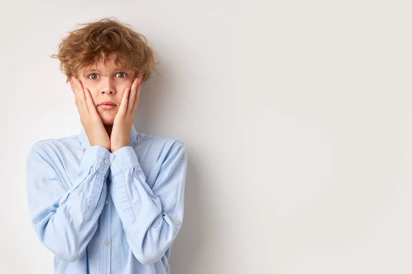 Bewildered curly caucasian boy holding cheeks and thinks — Stock Photo, Image