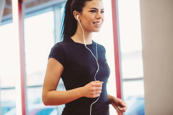 Nő fülhallgató fut beltéri pályán tornaterem — Stock Fotó