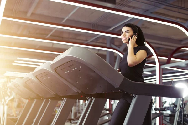 Mujer sonriendo mientras habla por teléfono móvil mientras se ejecuta en la cinta de correr — Foto de Stock