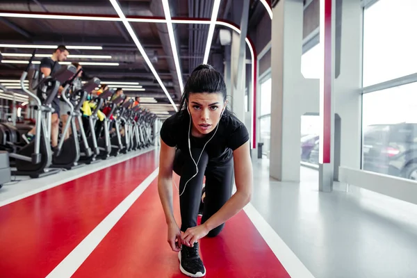 Ajuste menina para baixo para fazer cadarços no ginásio de fitness antes de correr treino de exercício — Fotografia de Stock