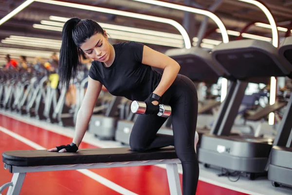 Femme flexion des muscles avec haltère sur banc dans la salle de gym — Photo