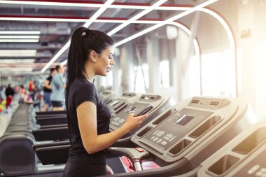 Genç Sporcu kadın koşu bandında koşarken akıllı telefon kullanıyor.