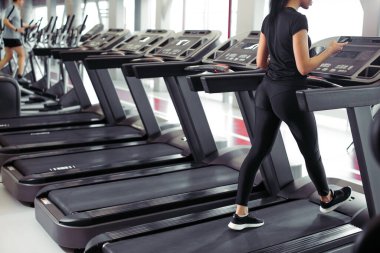 Sporcu kadın koşu bandında koşarken egzersiz uygulaması için akıllı telefon kullanıyor