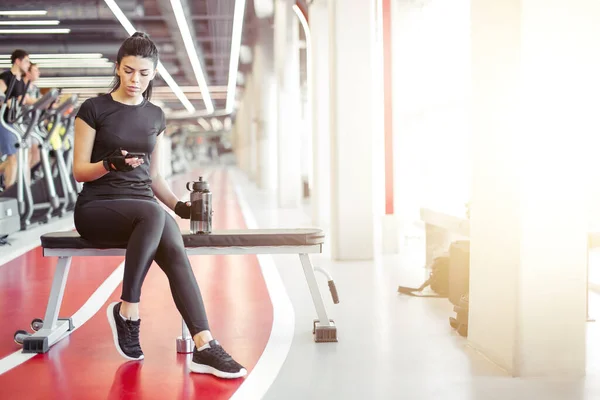 Fit femme avec bouteille en utilisant son téléphone intelligent avec écouteurs dans la salle de gym — Photo