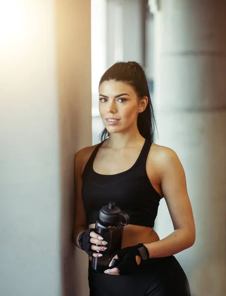 Modèle d'ajustement féminin posant avec de l'eau après l'entraînement près des fenêtres dans la salle de gym — Photo