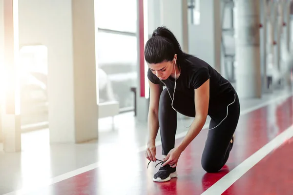 Жінка зав'язує шнурки у фітнес-центрі перед бігом на біговій доріжці — стокове фото