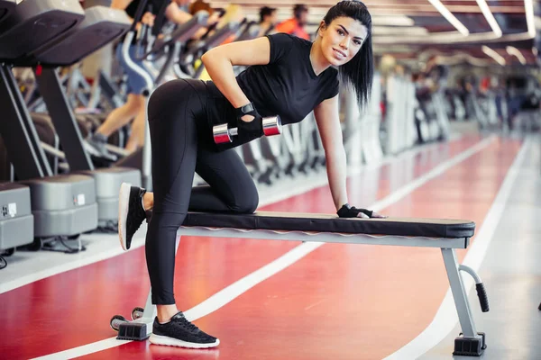 Femme flexion des muscles avec haltère sur banc dans la salle de gym — Photo