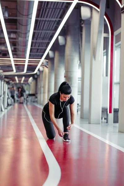 Mujer atando cordones de zapatos en el gimnasio antes de correr en pista de atletismo — Foto de Stock