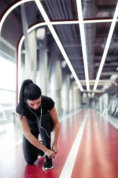 Mujer atando cordones de zapatos en el gimnasio antes de correr en pista de atletismo — Foto de Stock