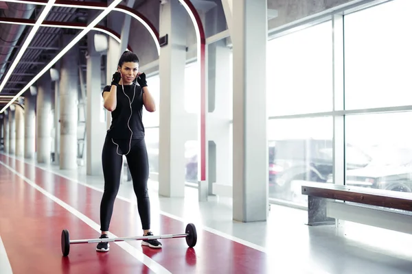 Fit jonge vrouw staan luisteren muziek in de sportschool met halters op de vloer — Stockfoto