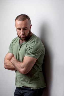 Sakallı, sıradan haki rengi tişört giyen, stüdyoda yalnız poz veren yakışıklı bir adam..