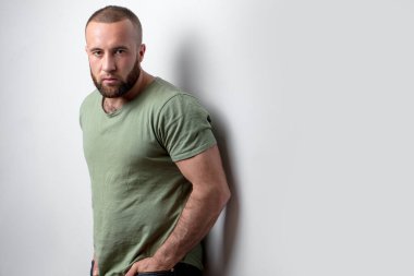 Sakallı, sıradan haki rengi tişört giyen, stüdyoda yalnız poz veren yakışıklı bir adam..