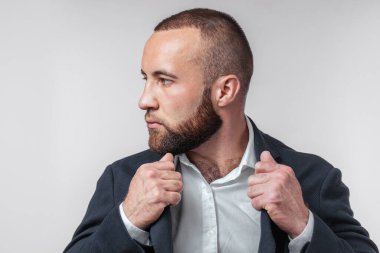 Resmi takım elbiseli sakallı genç adam beyaz arka plandan kameraya bakıyor.