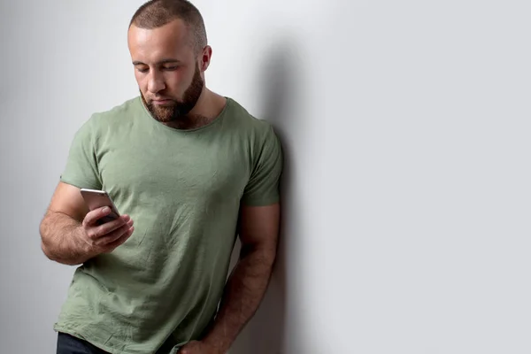Barbudo hombre en ropa casual mirando el teléfono sobre fondo blanco — Foto de Stock