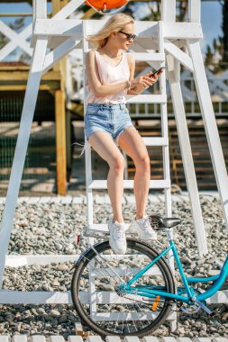 Genç bir kadın çakıl taşı plajında hızla bisiklet sürdükten sonra dinleniyor. Rahatlama kavramı