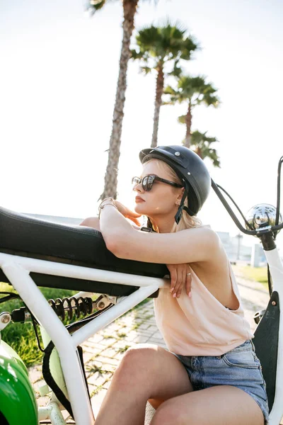 헬멧을 쓰고 보호용 안경을 쓰고 있는 소녀는 전기 자전거 가까이에 앉아 있다 — 스톡 사진