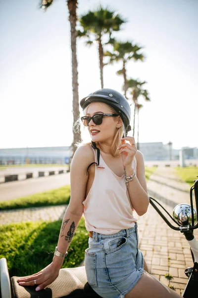 Chica joven con casco y gafas de protección se sienta cerca de la bicicleta eléctrica —  Fotos de Stock