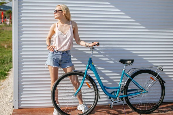 Jovem mulher bonita sentada em sua bicicleta com flores ao pôr do sol. Verão e estilo de vida — Fotografia de Stock