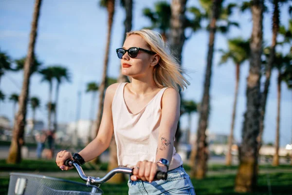 Mujer rubia alegre montar en bicicleta en el parque divirtiéndose en la tarde de verano — Foto de Stock