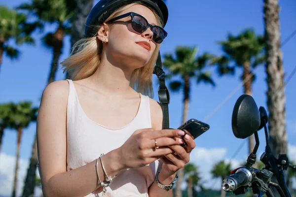 Atractiva mujer en casco de bicicleta con bicicleta eléctrica en el parque con teléfono — Foto de Stock