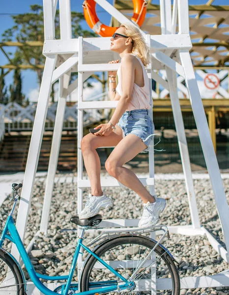 年轻女子骑自行车在卵石沙滩上快速骑完后休息。放松的概念 — 图库照片