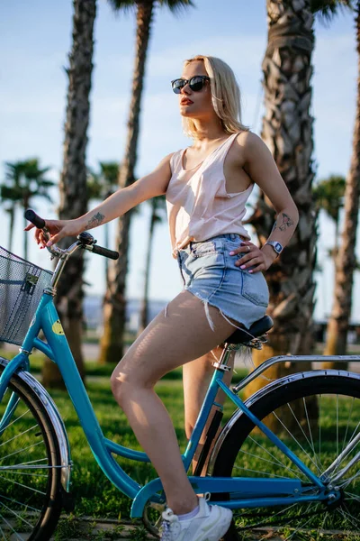 Mujer rubia alegre montar en bicicleta en el parque divirtiéndose en la tarde de verano —  Fotos de Stock