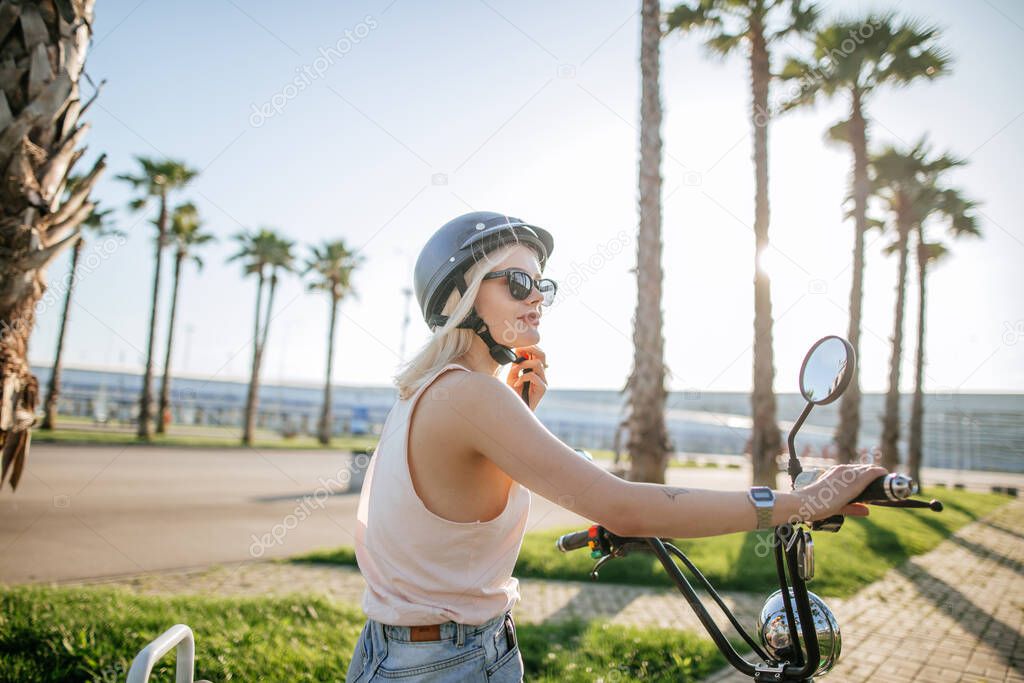 Young girl wearing helmet and protective glasses sits near electric bicycle