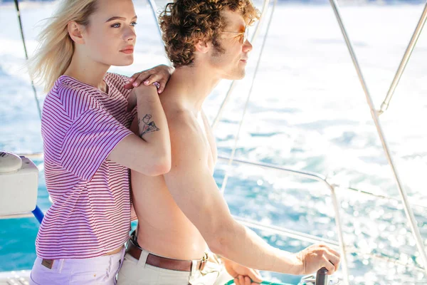 Muž se svou přítelkyní drží kormidlo jachty a dívá se daleko — Stock fotografie