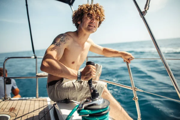 Низкий угол обзора молодого бородатого человека, стоящего на носовой яхте — стоковое фото