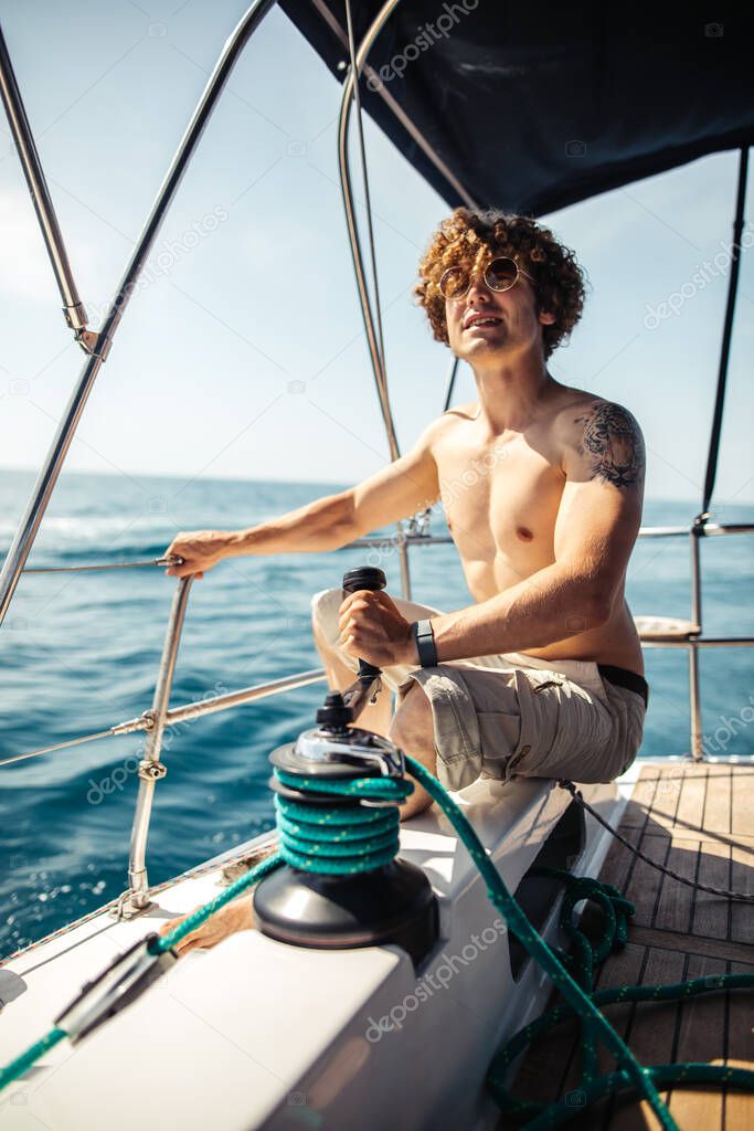Low angle view of young bearded man standing on the nose yacht