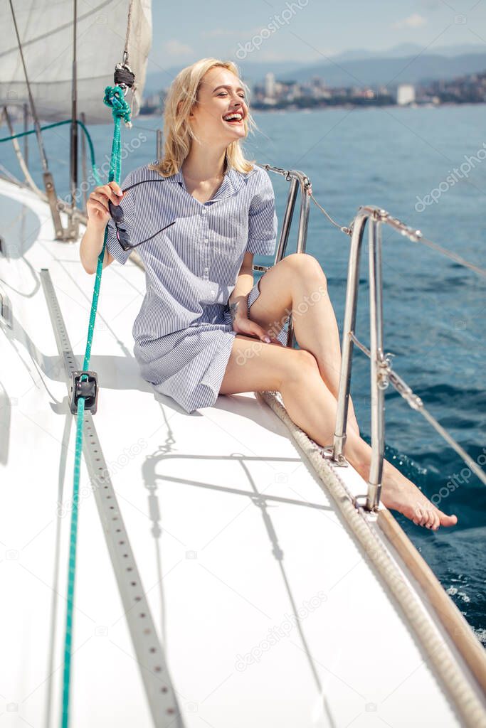 Woman on white yacht in nautical theme in open sea. Blond hair and blue clothes.