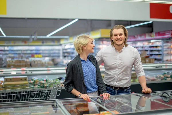 happy caucasian couple choosing frozen food at grocery store in shopping mall.