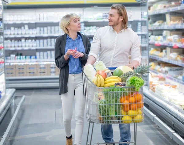 Мужчины и женщины толкают корзину с продуктами в проходе супермаркета — стоковое фото