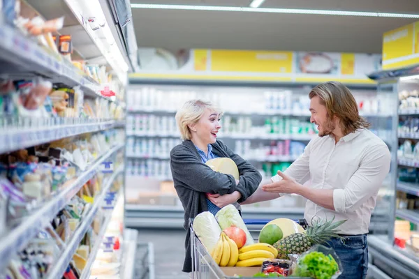 Mannelijke en vrouwelijke shoppers duwen kar met kruidenierswaren in supermarkt gangpad — Stockfoto