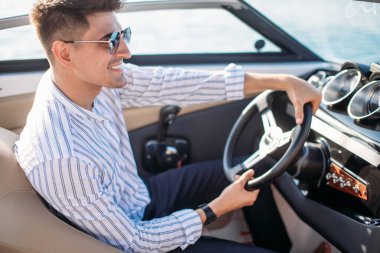 Lüks tekne ve yatların yanında duran başarılı bir işadamı mavi gökyüzüne karşı ceketini omzunun üzerinde tutuyor..