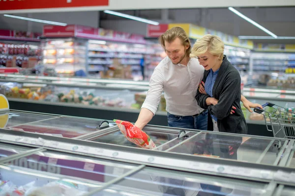 Счастливая кавказская пара выбирает замороженные продукты в продуктовом магазине в торговом центре. — стоковое фото