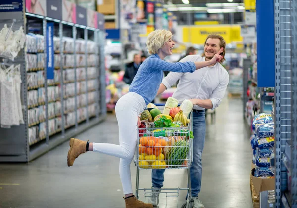 Pareja disfrutando de las compras en el supermercado. La mujer se trata de besar a un hombre —  Fotos de Stock