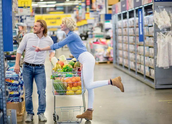 Par njuter av shopping i snabbköpet. Kvinna handlar om att kyssa en man — Stockfoto