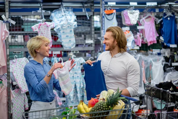 Casal feliz escolher roupas infantis no centro comercial. — Fotografia de Stock