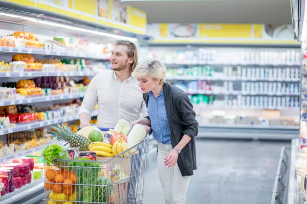 Casal em um supermercado de compras com carrinho cheio de alimentos comprando mantimentos — Fotografia de Stock