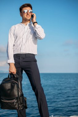 Güneş gözlüklü bir adam yat kullanıyor ve telefonda konuşuyor.