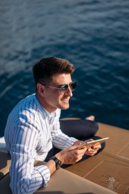 Deniz gezisindeki iş adamı, teknede tablet bilgisayar okuyor. Modern teknoloji, başarılı yaşam tarzı.