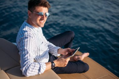 Deniz gezisindeki iş adamı, teknede tablet bilgisayar okuyor. Modern teknoloji, başarılı yaşam tarzı.