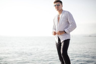 Güneş gözlüklü ve son moda elbiseli bir adam motorlu teknede yelken açıyor.