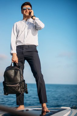 Güneş gözlüklü bir adam yat kullanıyor ve telefonda konuşuyor.