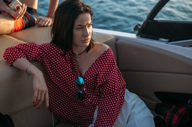 Güneşli bir yaz gününde yatta poz veren bikinili ve güneş gözlüklü genç bir kız.