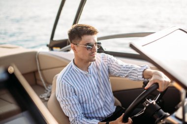 Lüks tekne ve yatların yanında duran başarılı bir işadamı mavi gökyüzüne karşı ceketini omzunun üzerinde tutuyor..