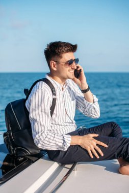 Güneş gözlüklü bir adam yat kullanıyor ve telefonda konuşuyor.