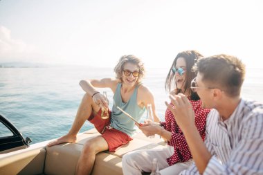 Yat bira içerken sohbet eden bir grup arkadaş yelkenli teknede parti veriyor.