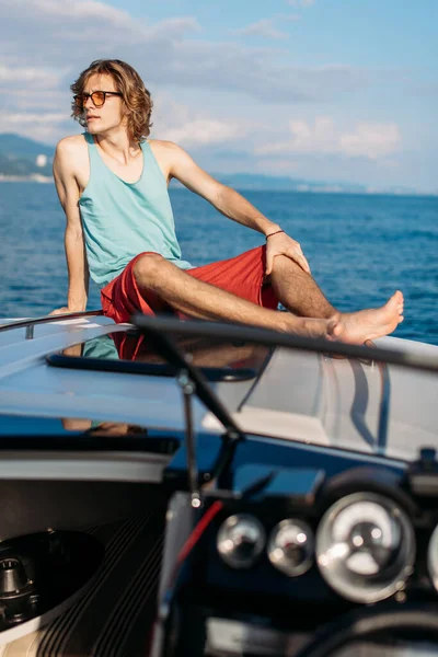 Joven chico hipster caucásico disfrutando de viaje en cubierta de yate navegando por el mar. — Foto de Stock